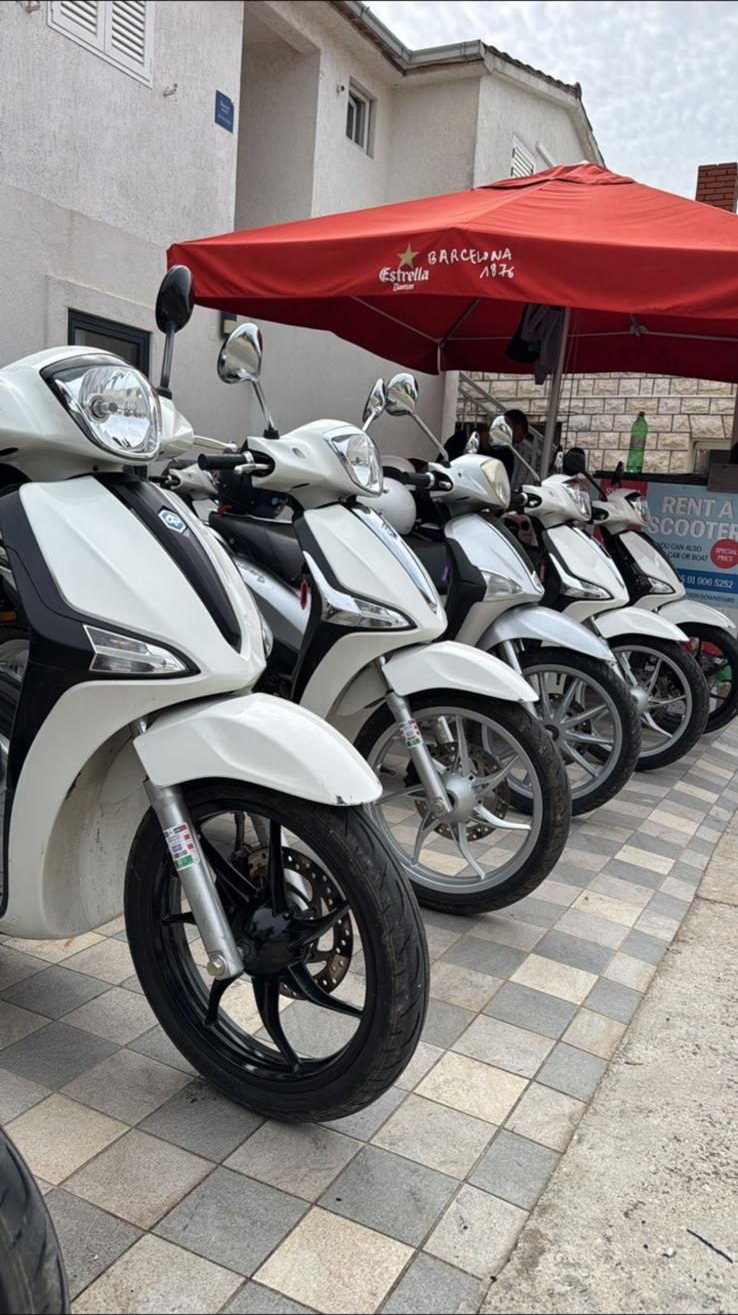 A row of white Piaggio Liberty 50cc scooters parked outside the hostel