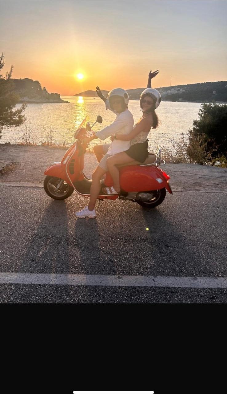 Two riders on a red Vespa on a coastal road above Hvar at sunset